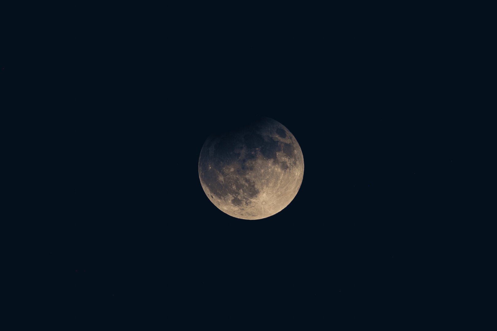 Lunar eclipse in early evening. The top of the moon is partially shadowed. The sky still has a dark blue hue as its still dusk when this photo was taken.
