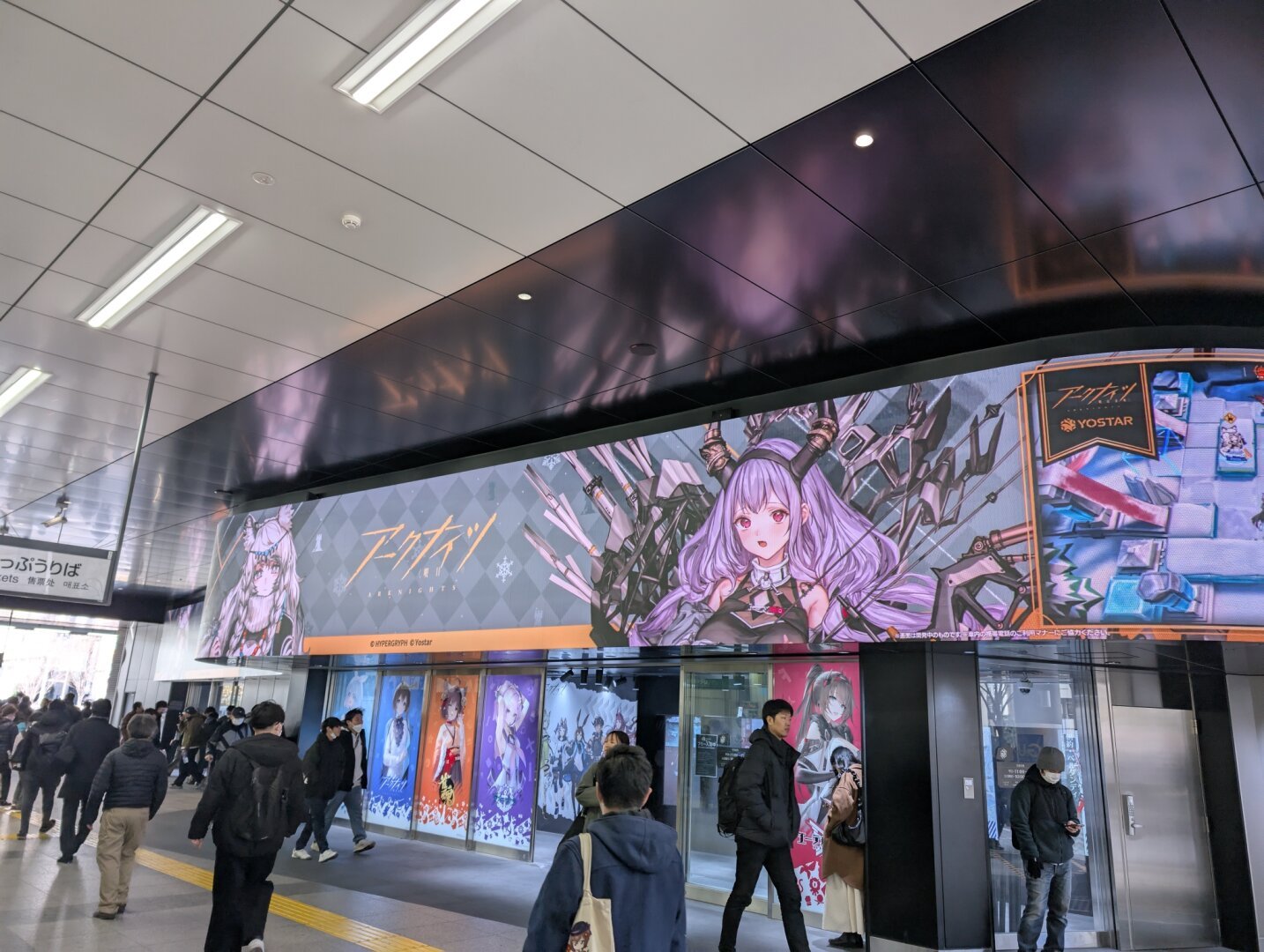 A large video display near an Akihabara train station with an ad for an anime game playing on it.