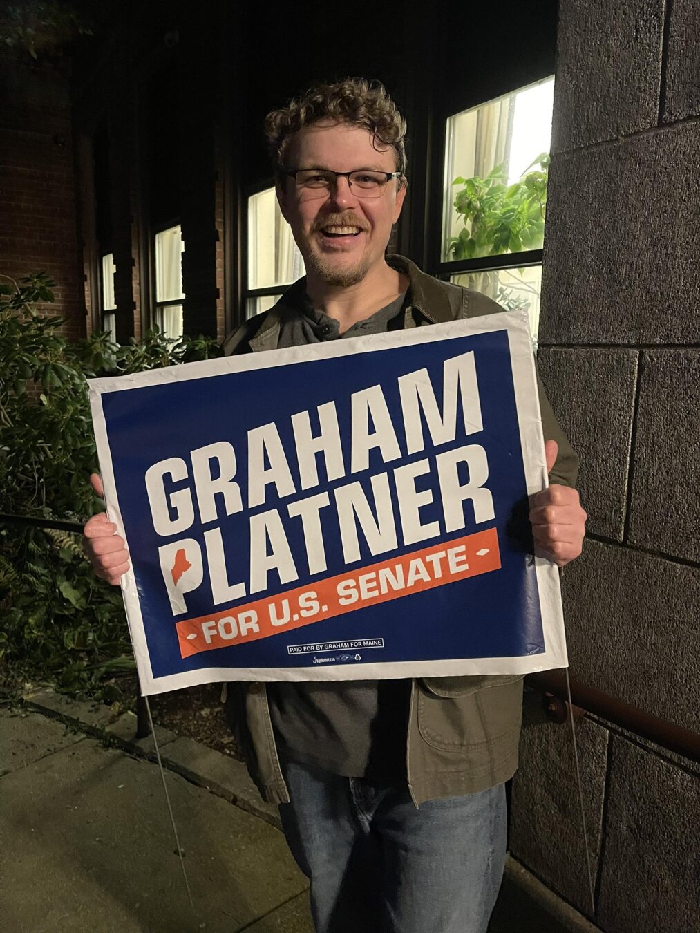 Gardiner Bryant holding a Graham Platner yard sign.