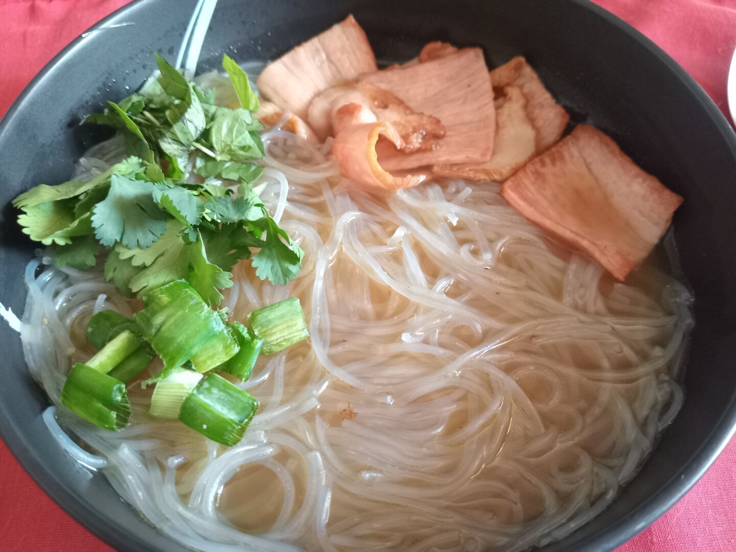 A plate of pho with basil, cilantro, and green onions