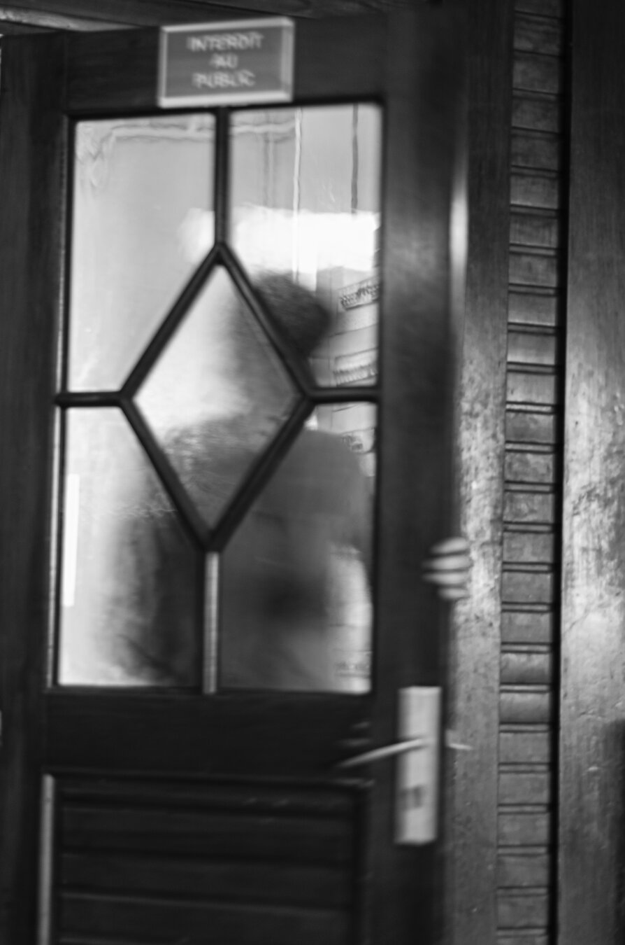 Silhouette derrière une porte vitrée. On voit la main qui ouvre la porte. Photo en noir et blanc