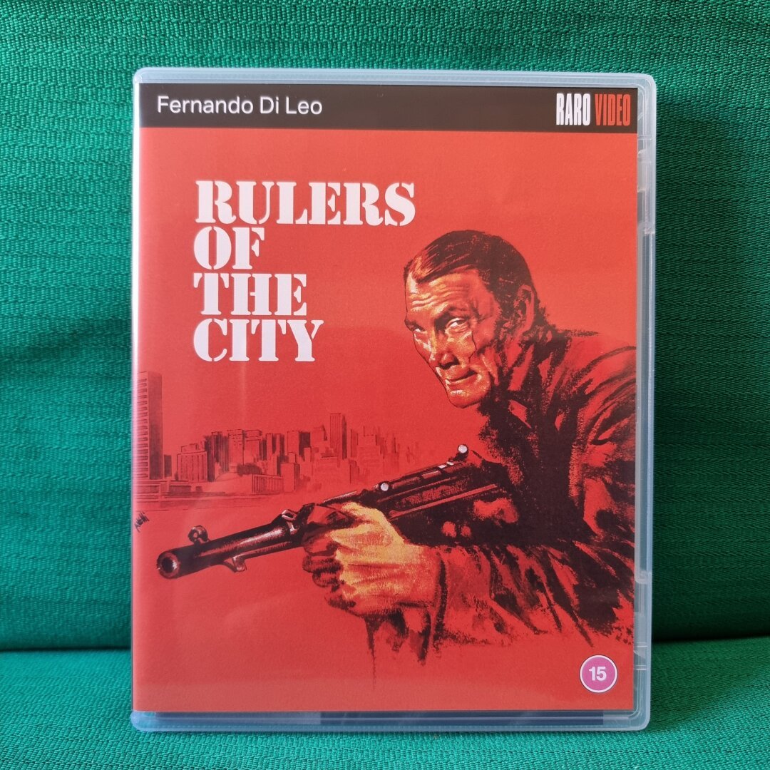 Showing the front cover artwork of the release (a drawn artwork showing a guy holding a machine gun and the sillhouette of a skyline in the back).