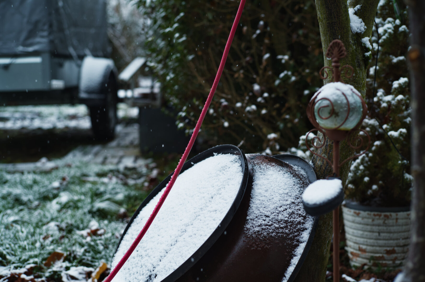 Snow in the backyard with some gardening pots, and a red cable.