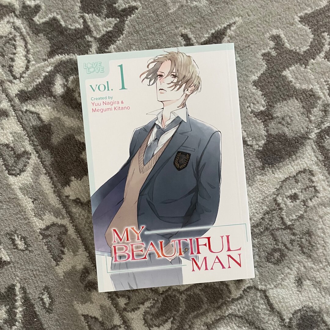 A manga volume is shown against a grey rug.