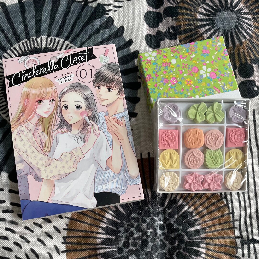 A manga volume is shown next to some pretty Japanese sweets.