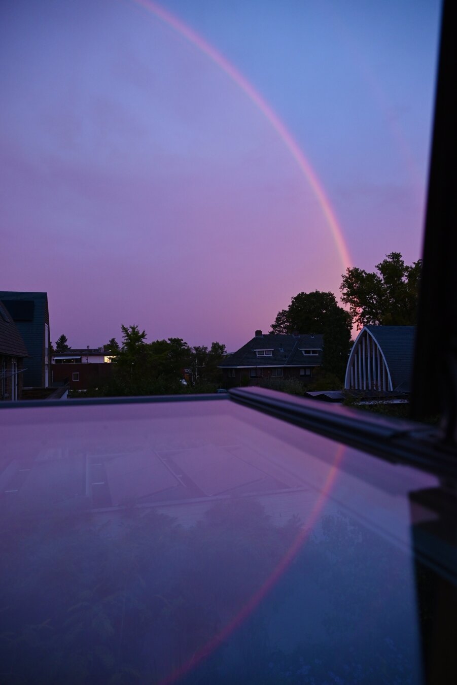 Rainbow in a pink-blue morning sky, reflected in a window.