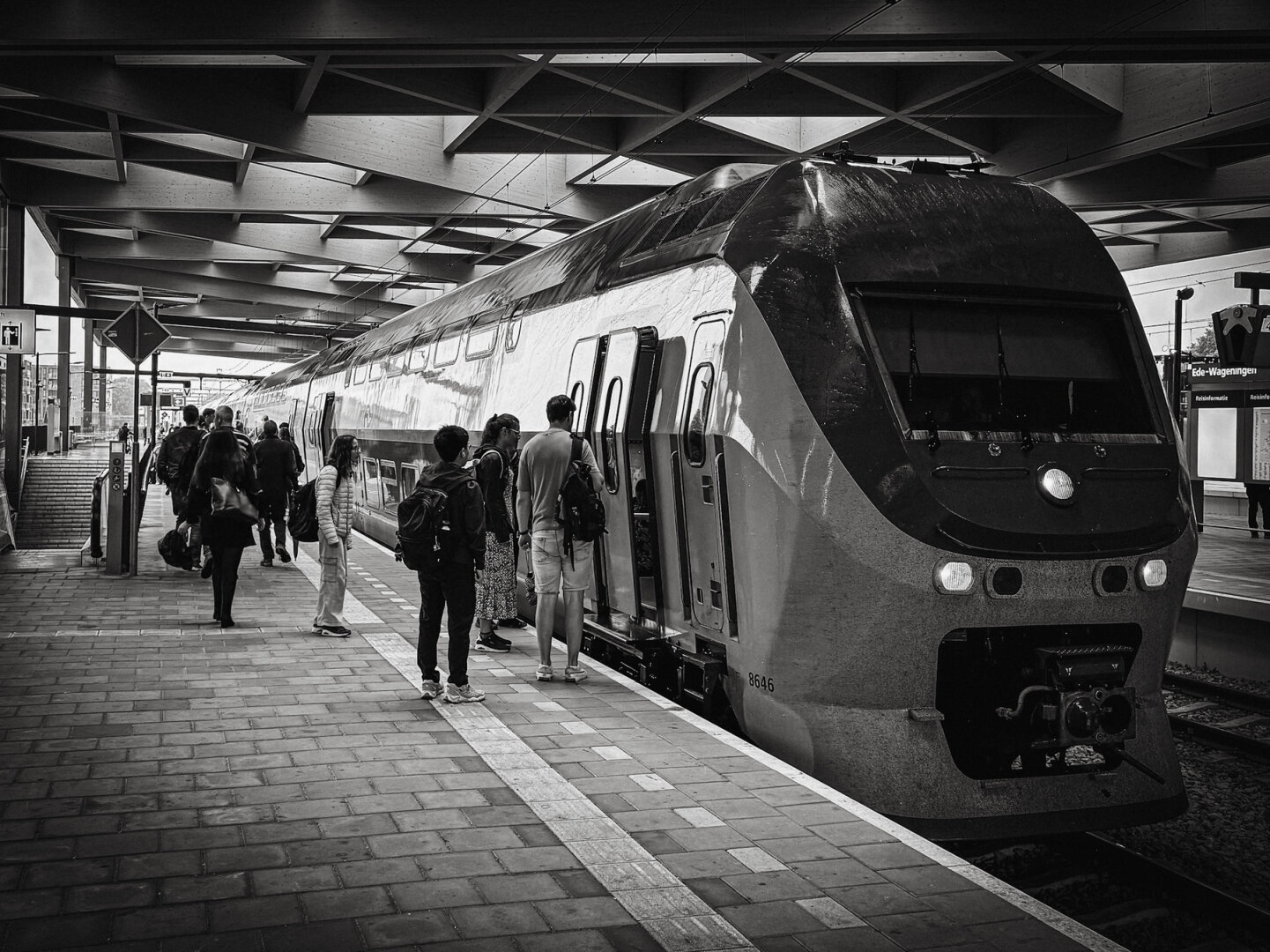 Dutch train on a platform, with people waiting to get in. In black and white.