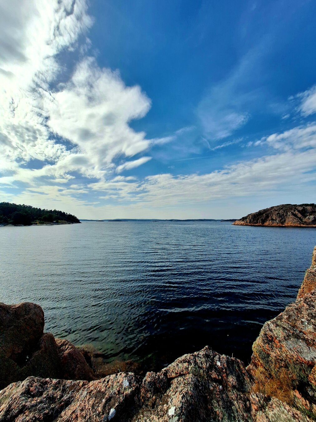 View over a small bay in Southwest Sweden. Some white clouds are visible in a clear blue sky above the water.