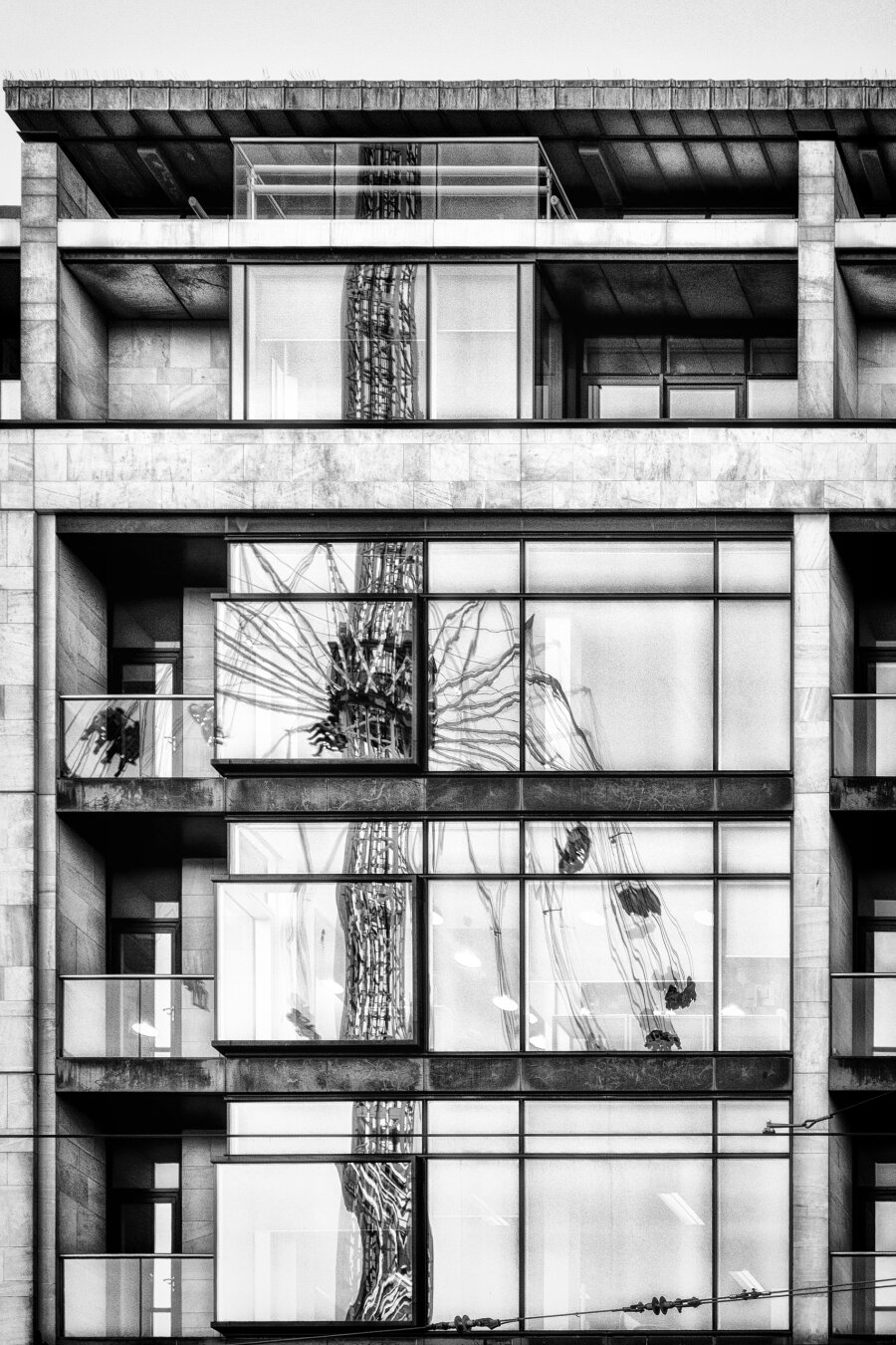 Eine vertikale Schwarz-Weiss-Aufnahme fängt die Fassade eines modernen Gebäudes in Edinburgh ein. Die Fenster reflektieren abstrakt die Struktur eines Kettenkarussels. Klare Linien und starke Kontraste betonen die grafische Qualität der Komposition.