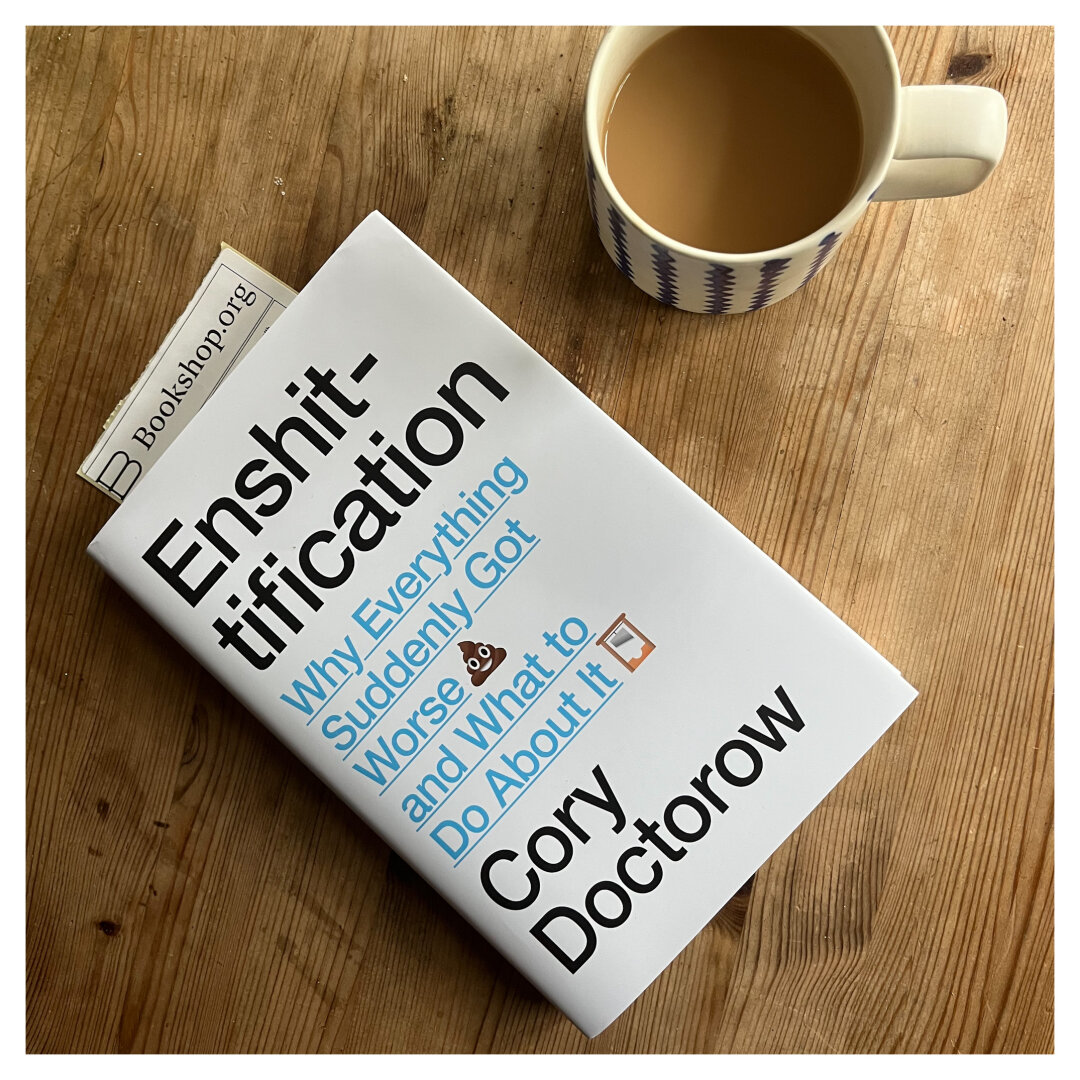 A copy of Cory Doctorow’s “Enshittification - why the world suddenly got worse and what to do about it” photographed from above on wooden table next to a mug of tea.