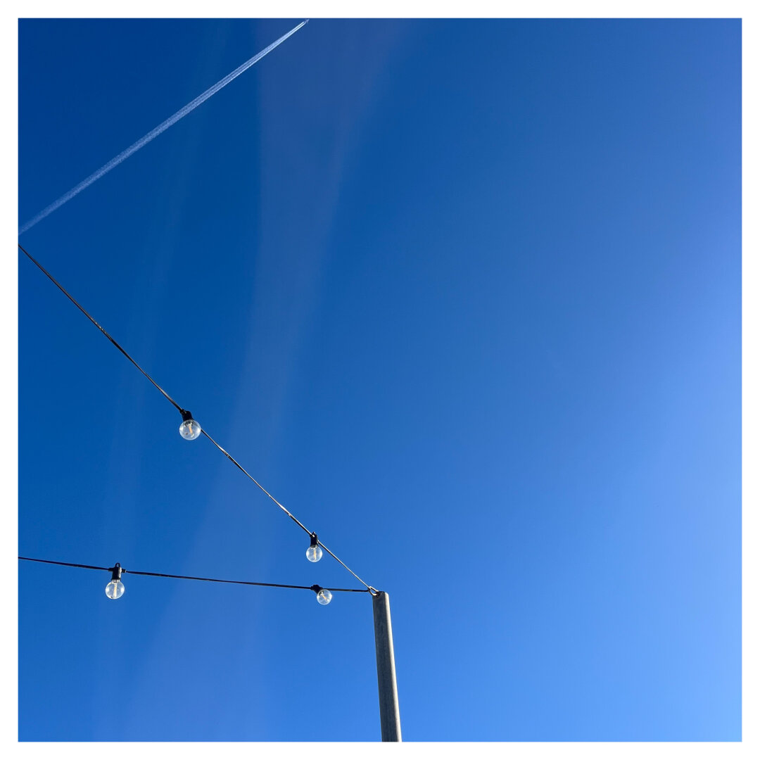 A clear blue sky with the bottom left corner of the frame broken by some street-decoration lamps.