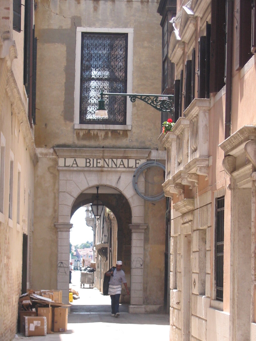 A narrow street. A man walks under an arch with la biennale written above it.