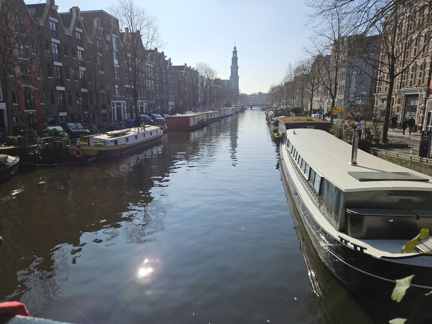 view down a canal in Amsterdam with narrow boats docked on both sides and a church in the background