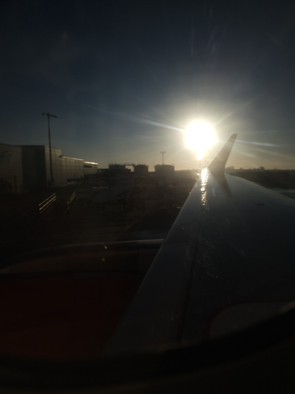 view of airport from wing with the sun rising over the end of the wing