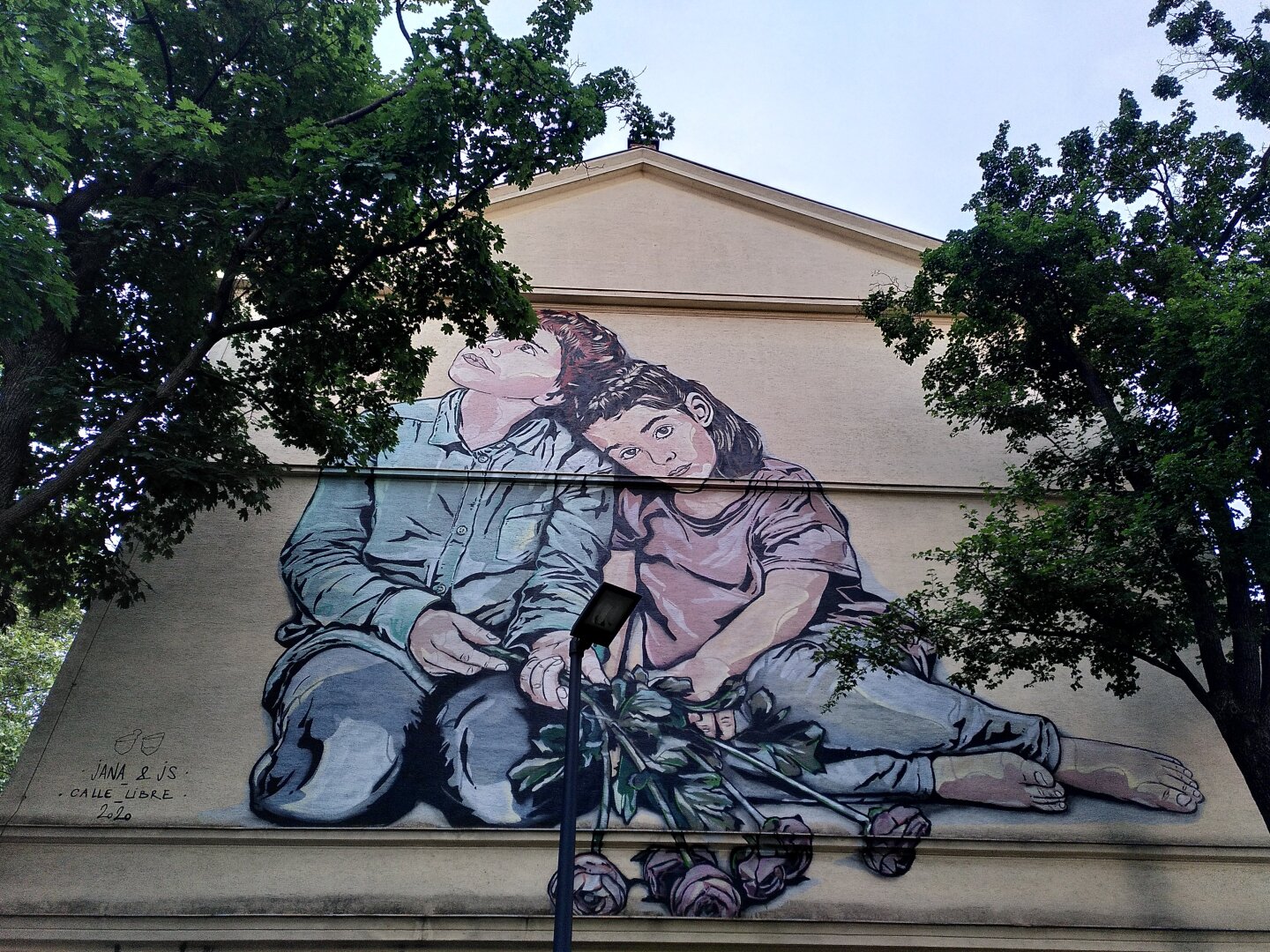 One boy and one Girl are sitting next to each other. The boy is looking into the sky, while the girl is looking straight to the viewer. She is holding 6 roses in her hand.