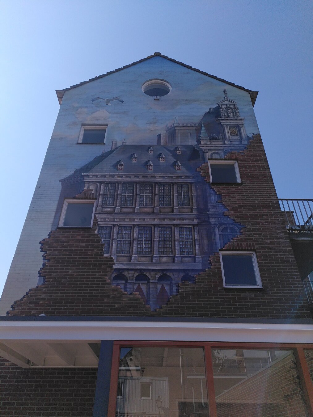 Old mansion, hidden between a red-bricked front painted on a wall of a house, you can also see ablue sky with a seagull at the top of the house