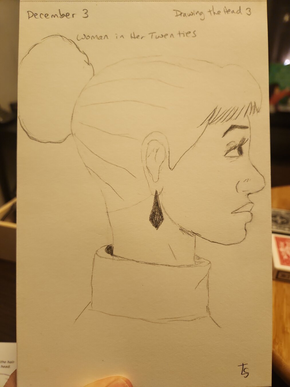 Pencil sketch of side view of "woman in her twenties." She is looking to the right and is wearing her long hair in a bun. She has prominent bangs and an earring. She's wearing a turtle neck sweater.