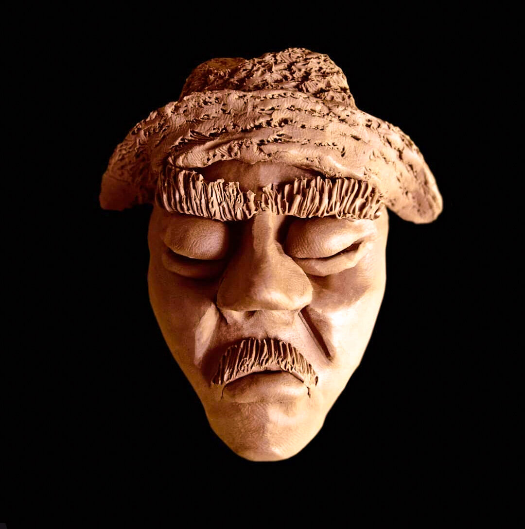 This is a sculpture depicting a weathered, elderly man's face with deeply expressive features. The portrait shows intricate detail in the wrinkled skin texture, with pronounced lines around the closed or nearly closed eyes and mouth area. The figure wears what appears to be a textured cap or hat with a rough, bark-like surface. The man has a full mustache and the overall expression conveys wisdom, weariness, or contemplation. The sculpture is photographed against a black background with dramatic lighting.