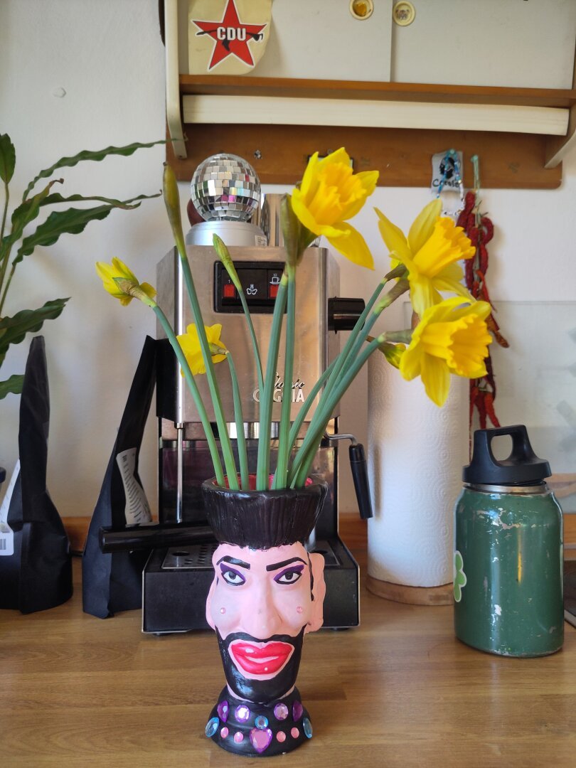 A vase resembling Harald Glöööckler, the German fashion designer. Inside are some yellow flowers.