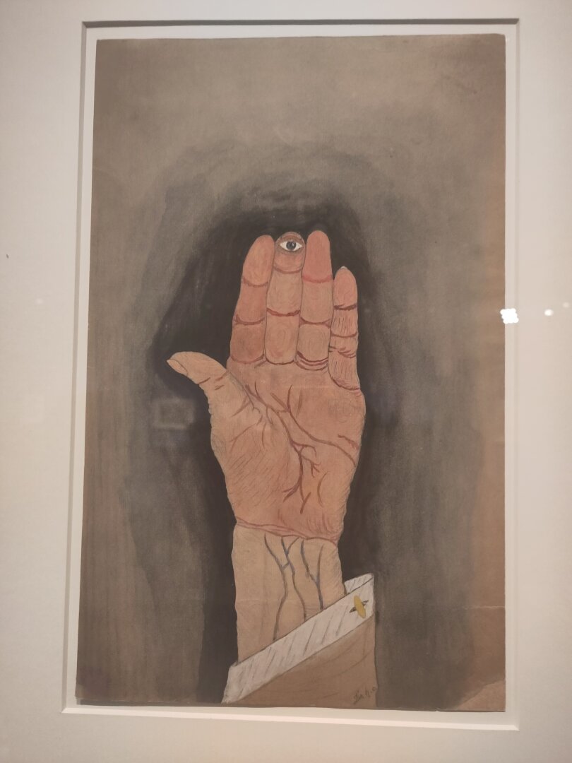 A photographed painting from an exhibition in the Prinzhorn Foundation in Heidelberg showing a hand of which the middle finger has an eye. It stares right at the viewer.