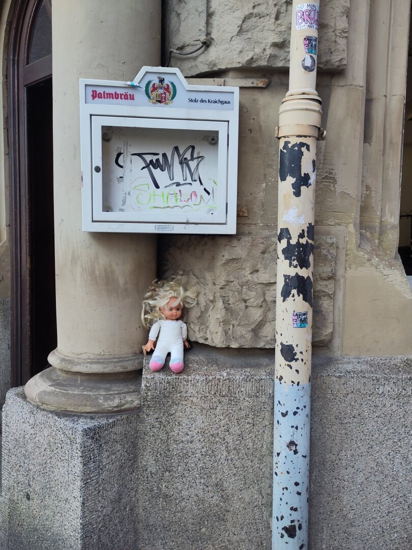 A dirty doll sitting on a wall in front of an abandoned looking restaurant.
