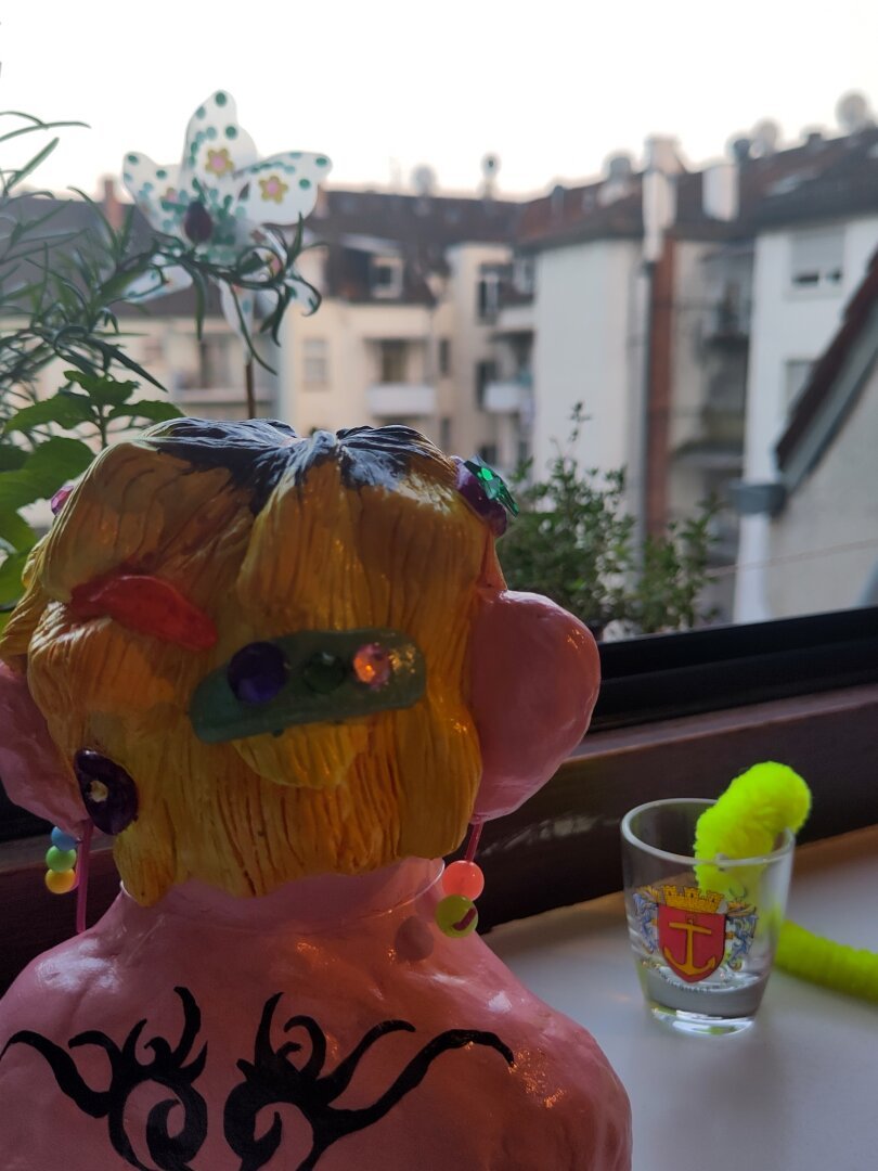 She's looking out of the window exposing her tattooed back. Her furry worm friend is drinking from a shot glass.