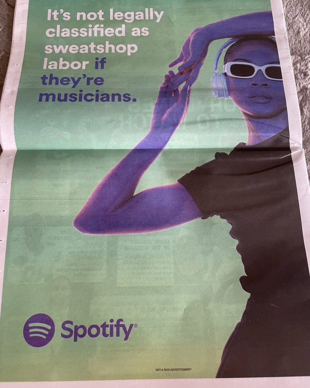 A full page advertisement for Spotify in The Onion shows someone wearing shades and headphones while dancing. 

Overlay text reads: It’s not legally classified as sweatshop labor if they’re musicians. 

Fine print at the bottom reads: Not a paid advertisement.