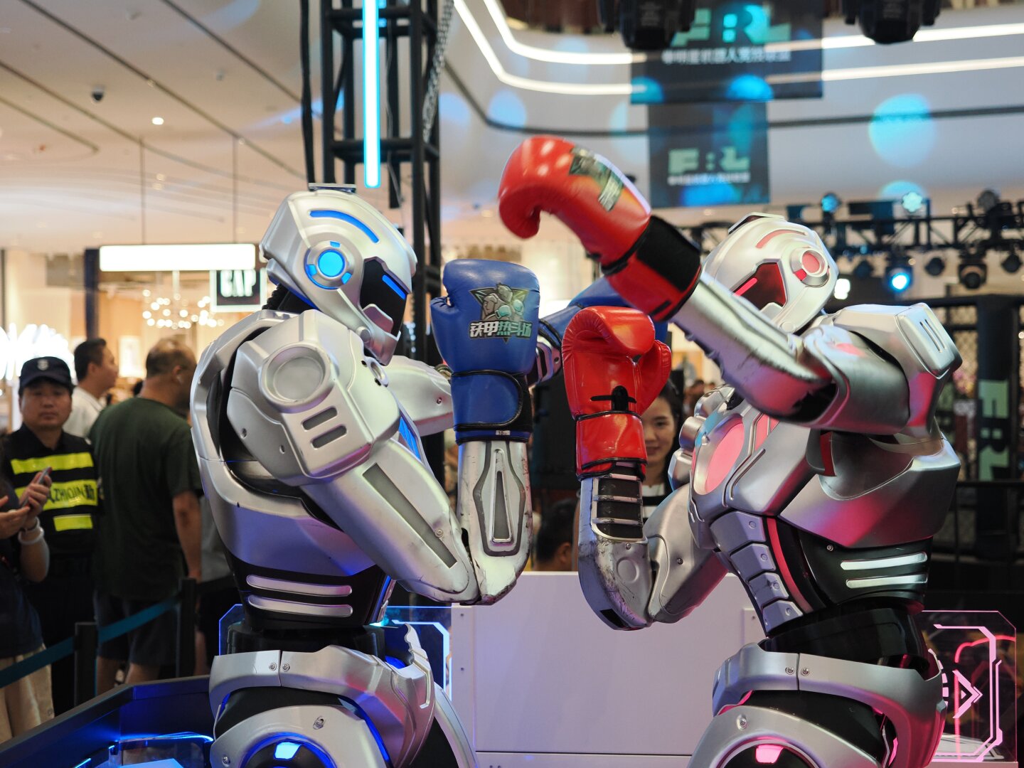 Two robots, one with red accents and red boxing gloves and one with blue accents and blue boxing gloves face each other. Both are trying to punch with their left hand