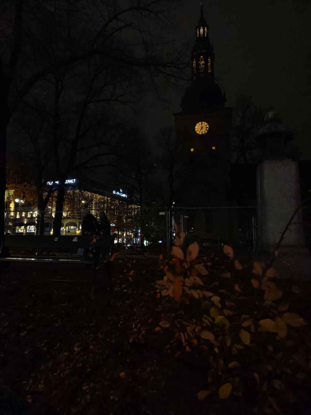 Центр Осло. Осень. Ночь. Виднеется силуэт церкви. Желтый круг циферблата башенных часов контрастирует с темно-серым фоном неба. И как будто подсвечивает желтый куст на переднем плане