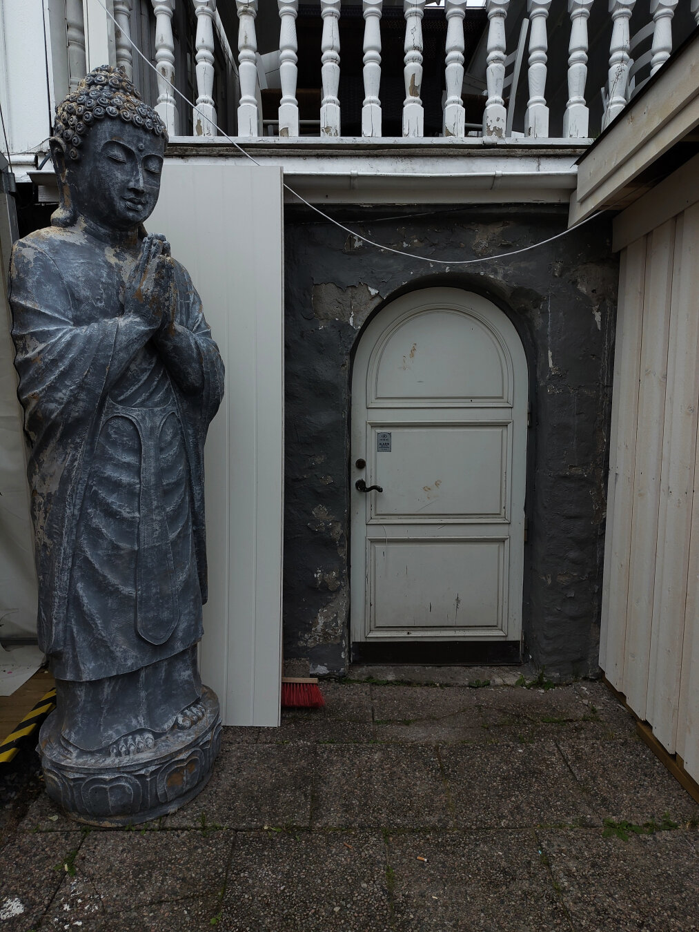 Статуя Будды с человеческий рост стоит слева от белой двери. Руки Будды сложены в молитвенном жесте, его голова слегка наклонена. Чтобы войти в дверь тоже придется склонить голову. Над дверью расположена терраса
