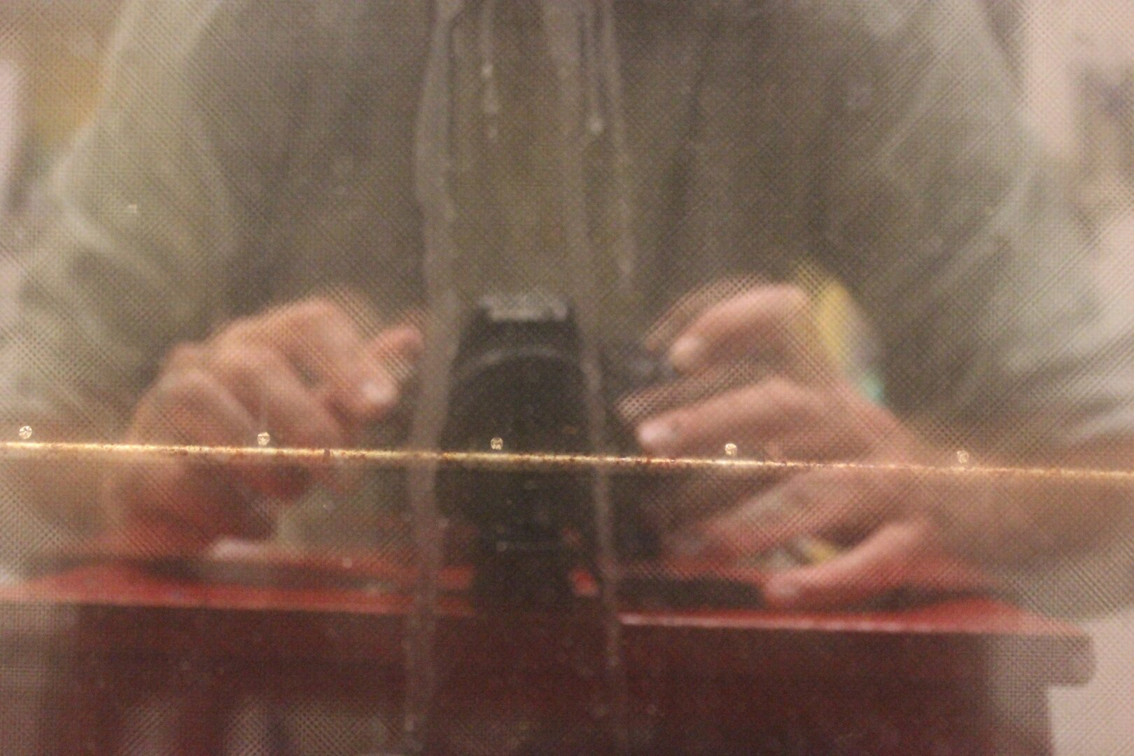 A reflection of a person taking a picture. It is blurry and a stain runs through the center. The fingers are spread