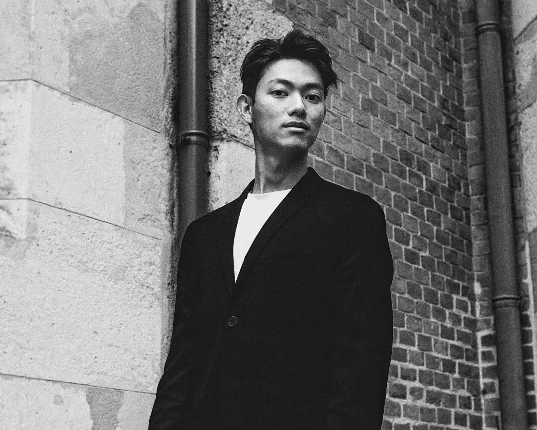 monochrome portrait of a young man standing in front of a wall