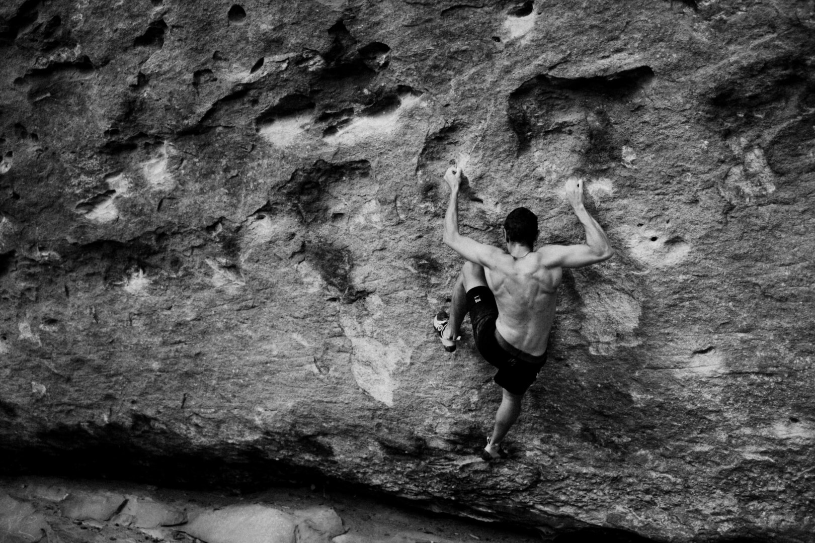A black and white photograph of a man bouldering.