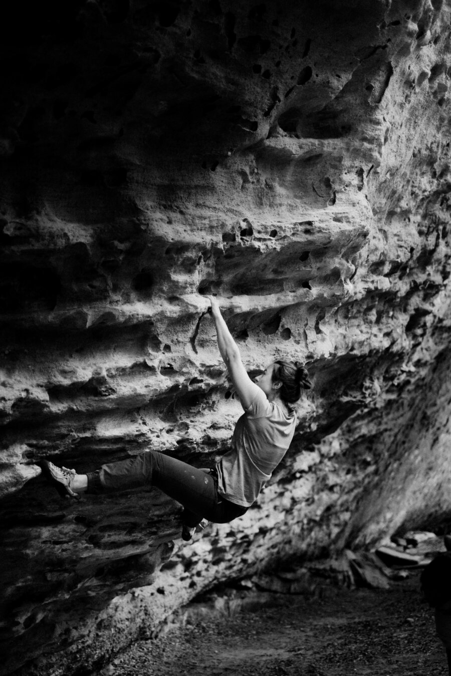 A black and white photograph of a woman bouldering.