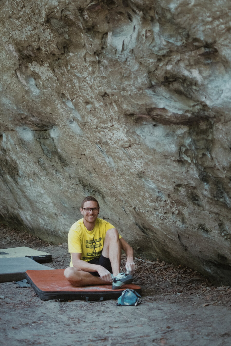 A man sitting on a boulder mat, tying his shoes.