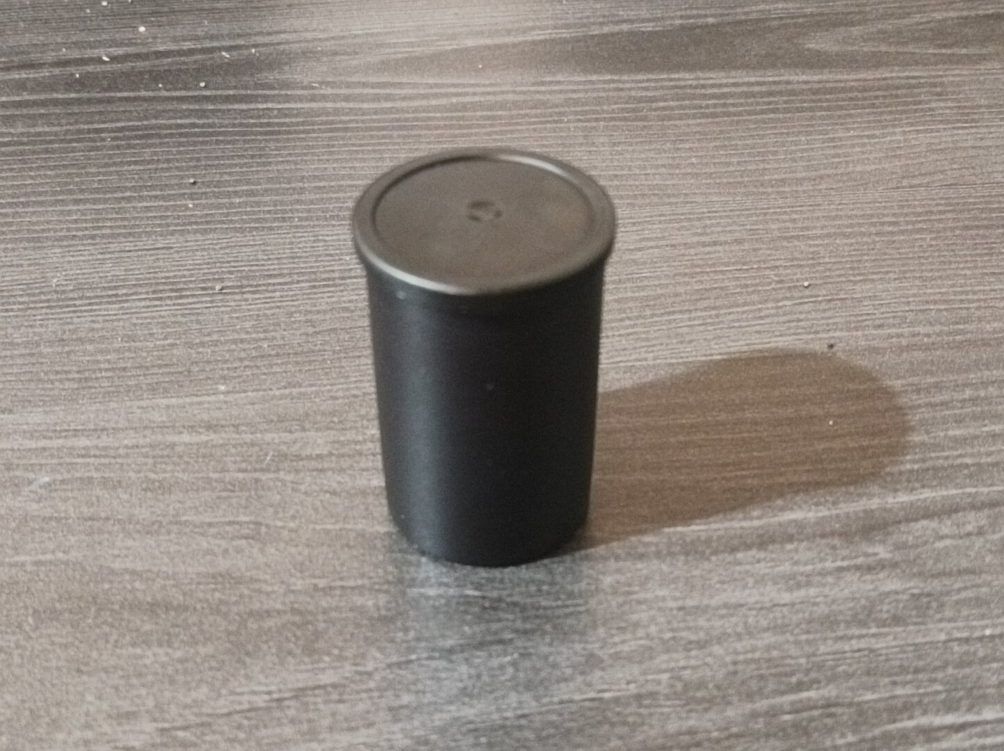 Picture of a black film roll container laid on a table with its lid closed.