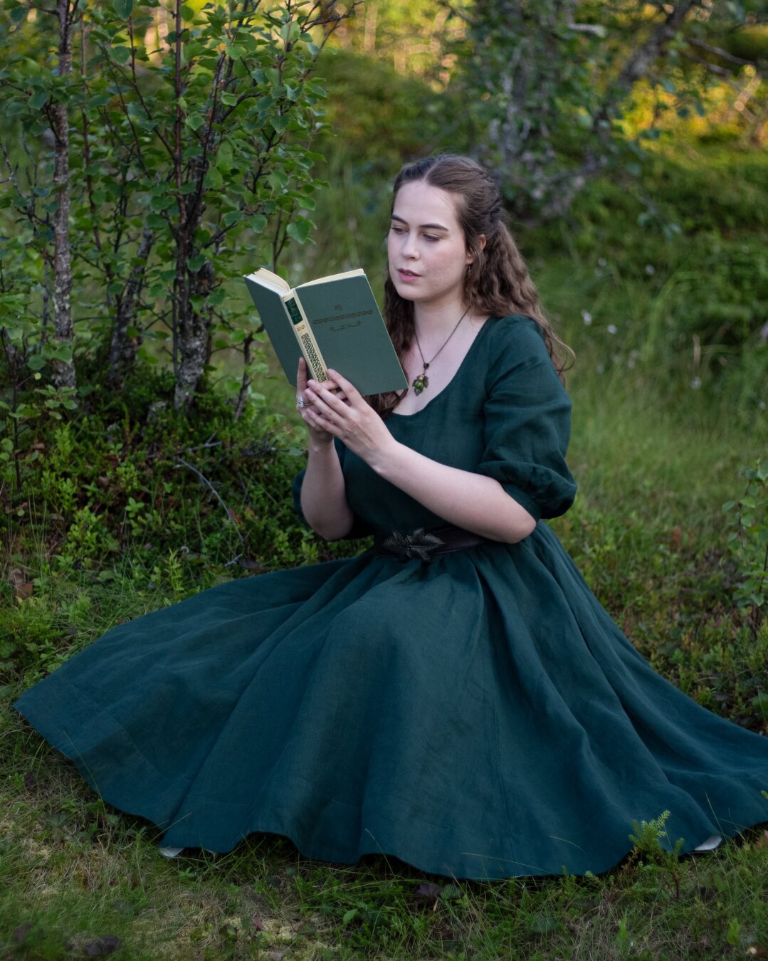 A woman in a green dress sitting in the forest and reading a book