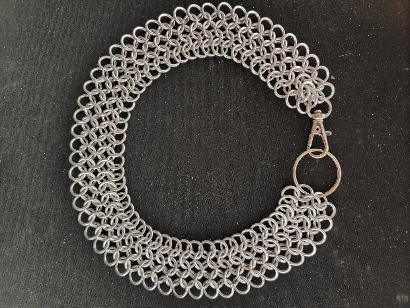 The chainmail choker described in the post laid flat. It is arranged in a circle and clasped. Photographed on top of a plain black background.