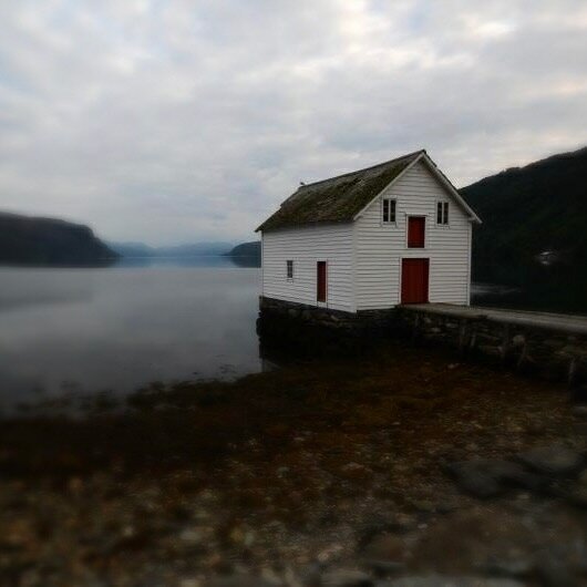 Et hvitt hus ytterst på en kaikant, i en vestlands fjord.