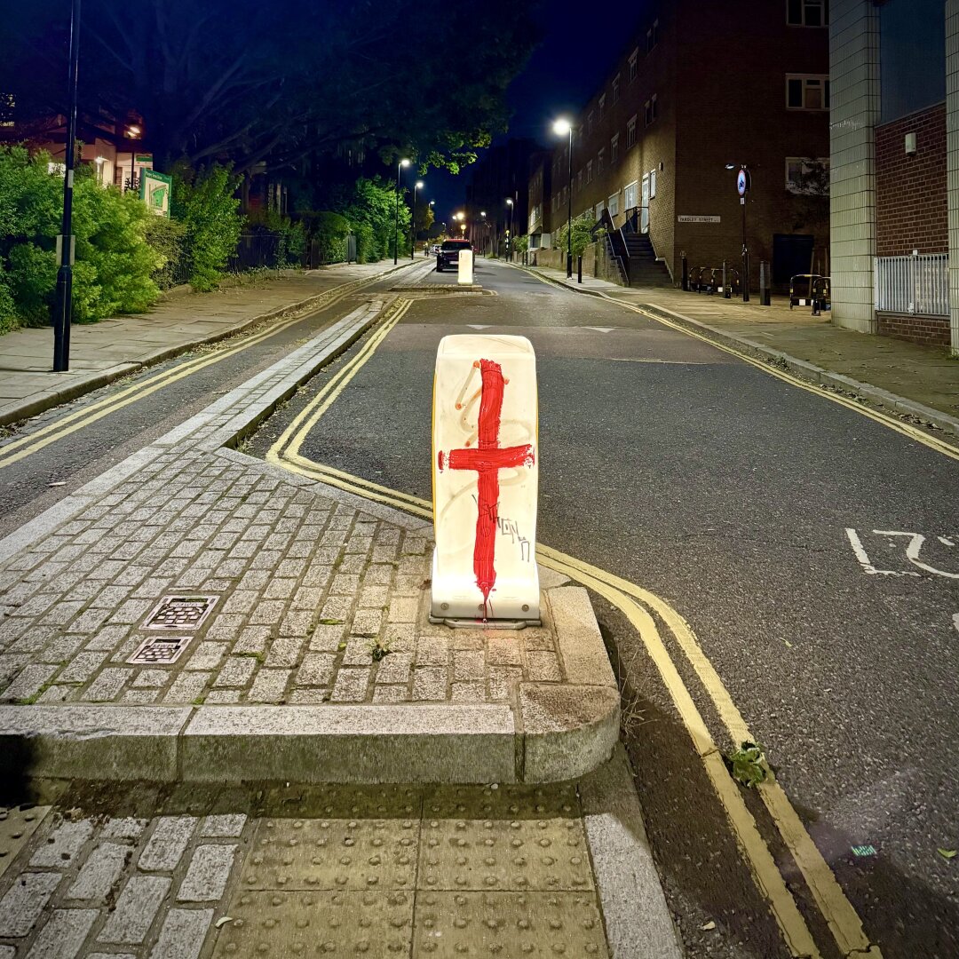 Night scene of a deserted street in Islington, a central London borough. Front and centre is a traffic bollard graffitied with St George’s cross, red on white, a symbol of delusional English nationalism.