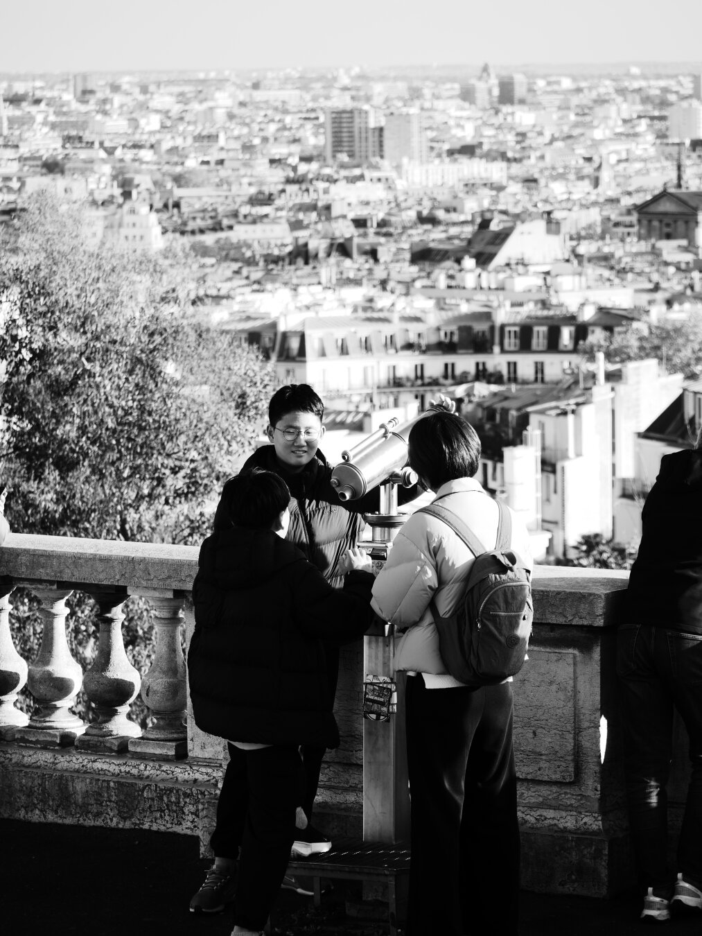 A black-and-white photograph of a family, they are around a spyglass to see the Great Paris, through a spyglass. This scene take place at the top of Montmartre hill