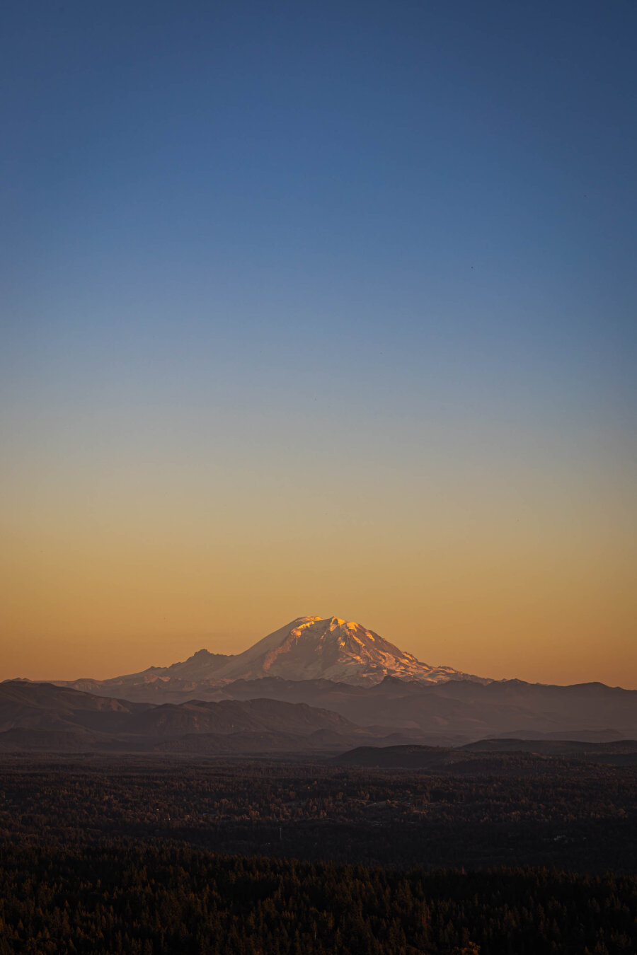 A vertical image of a mountain at sunset with layers of orange and blue.