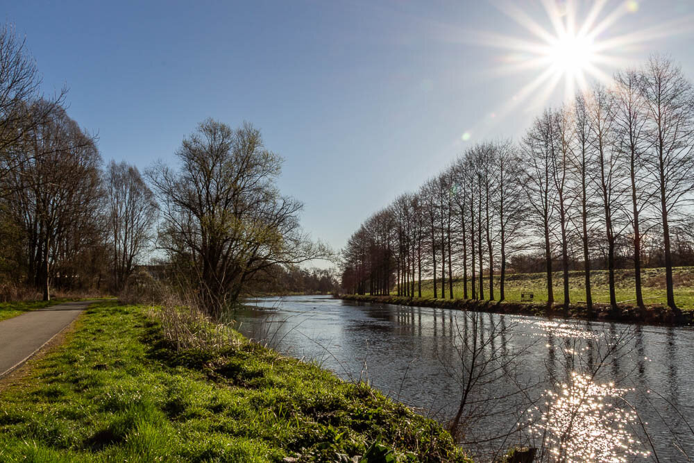 A bright morning scene by the Ruhr River with the sun shining in a clear blue sky. A path runs alongside the water, bordered by green grass and trees, while the sunlight sparkles on the river’s surface.
Ein heller Morgen am Ruhrufer mit strahlender Sonne unter blauem Himmel. Ein Weg verläuft entlang des Wassers, gesäumt von grünem Gras und Bäumen, während das Sonnenlicht auf der Wasseroberfläche glitzert.