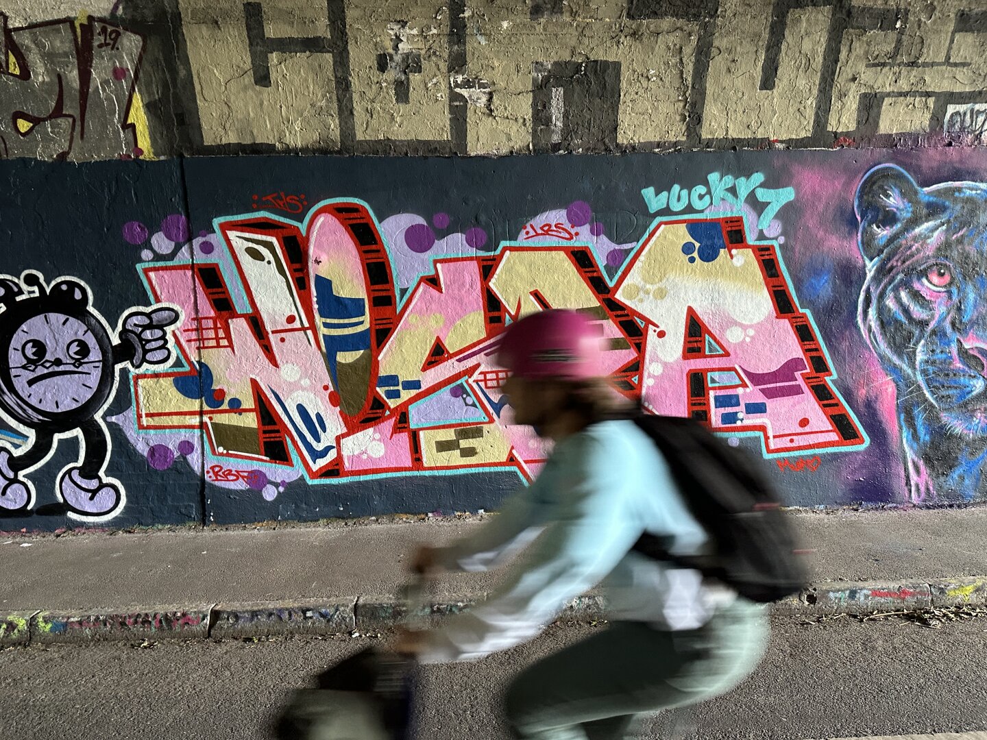 A cyclist Cycles in front of a colourful mural. The mural spells "wispa". The image of the cyclist is blurred from speed.