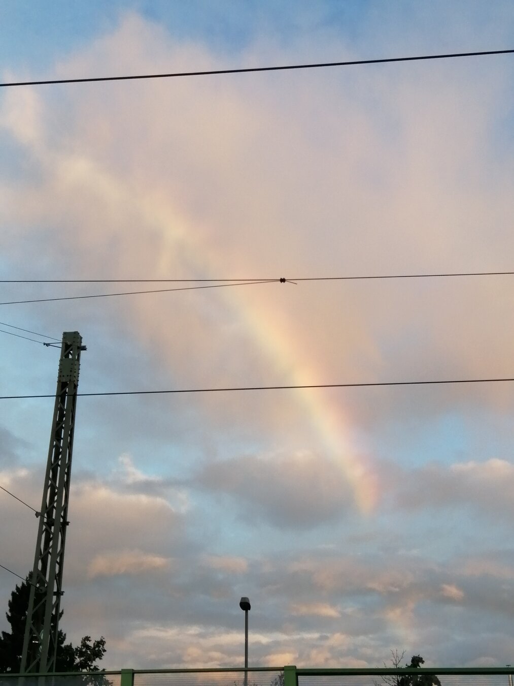 Regenbogen in den Wolken (die rechte Seite). Davor Oberleitungen.