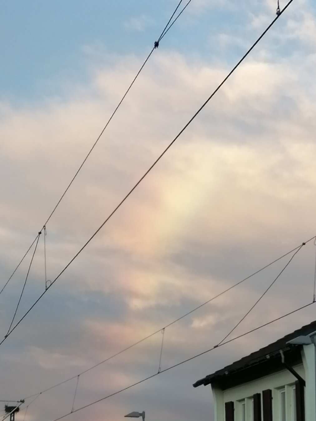Regenbogen in den Wolken. Davor Oberleitungen. Die linke Seite des Regenbogens, die etwas heller ist