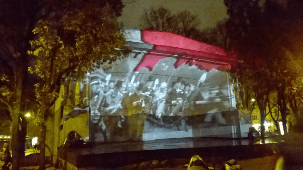 Still from a clip, showing groups of people in horse drawn carriages, with red bleeding from the top