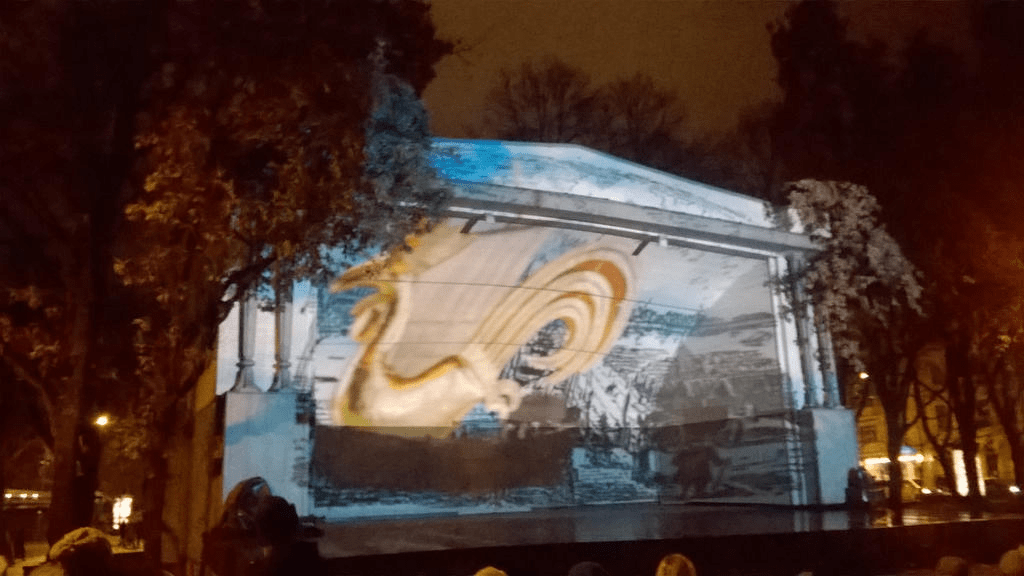 Golden Rooster moving by a blue hued Old Riga drawing