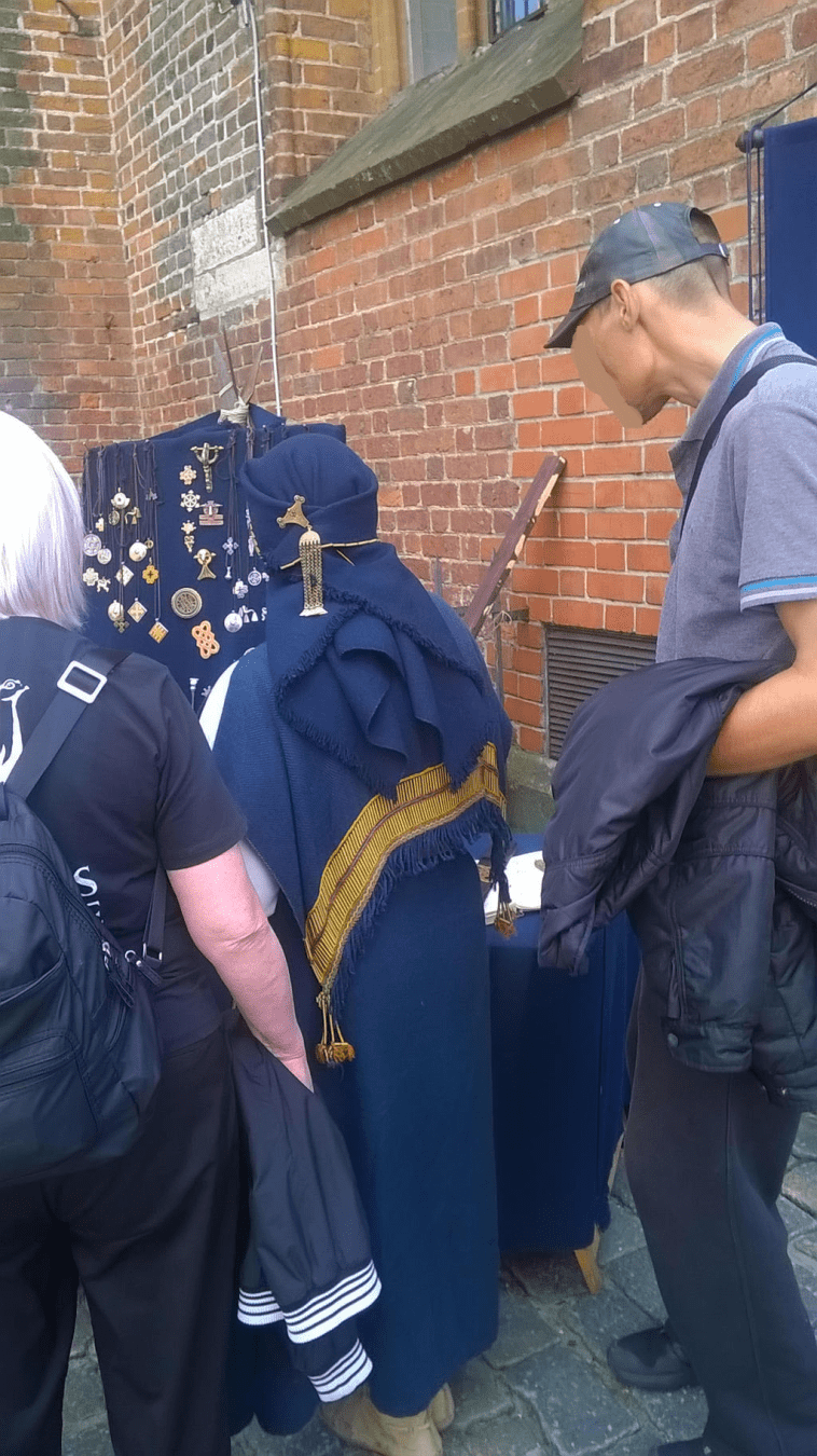Photo of a stall with traditional Latvian jewelry, with a lady in blue, the stall worker, showing some curious customers her wares