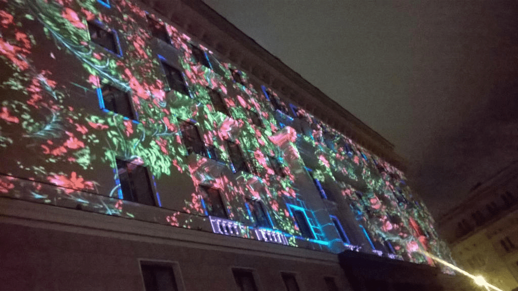 Front of a hotel, its facade lit up with flowers and leaves